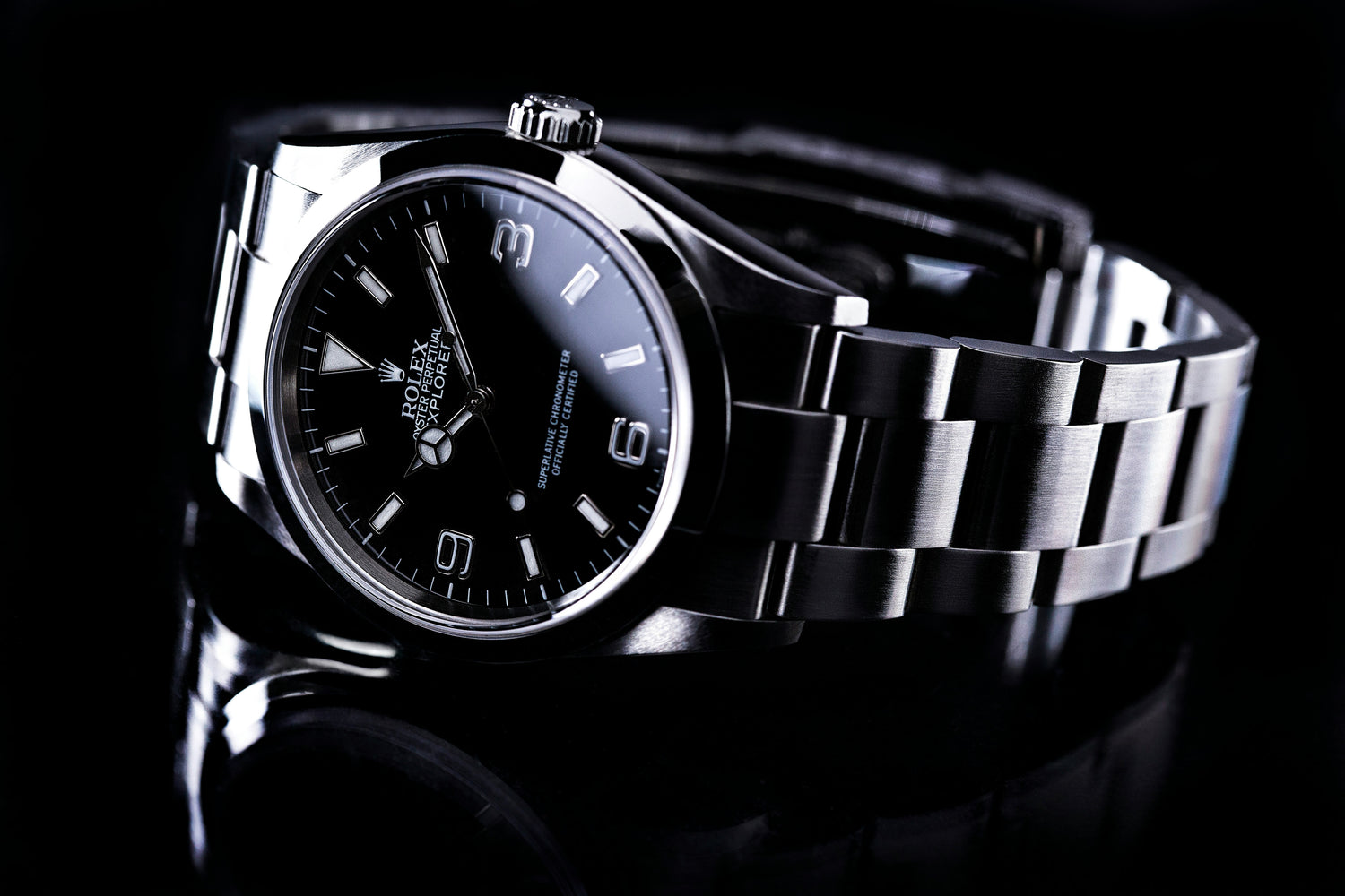 Close-up of Rolex Explorer watch with black dial and stainless steel bracelet, showcased against a reflective black surface.